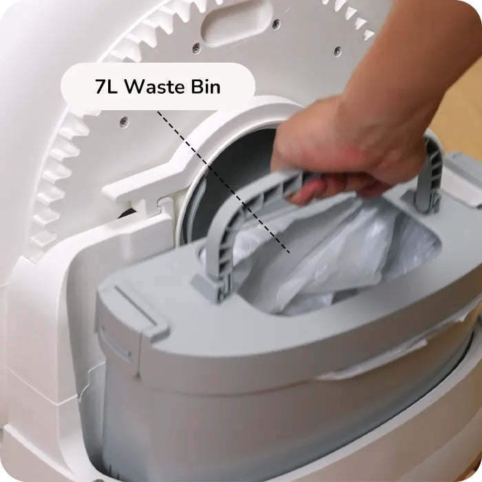 Hand pulling a 7 L waste bin out of a white automatic litter box.