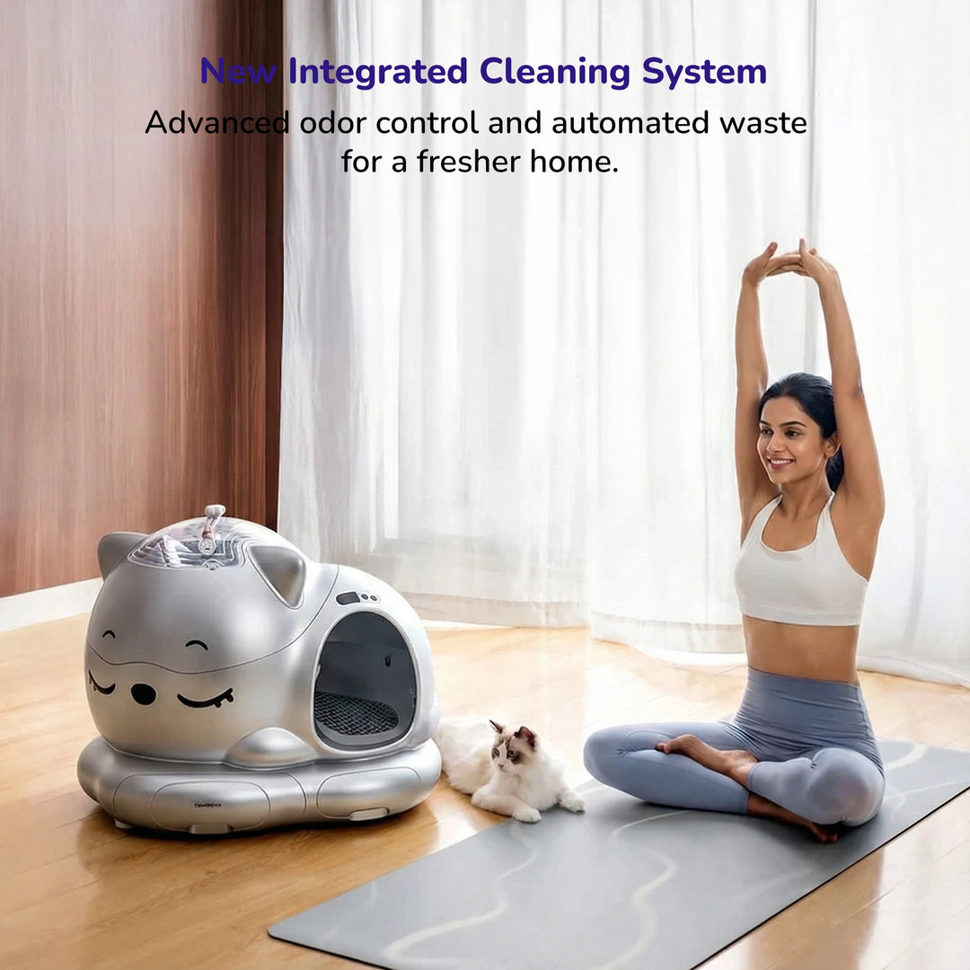 A silver smart cat litter box with a happy face design next to a stretching woman and a relaxed cat in a bright living room.